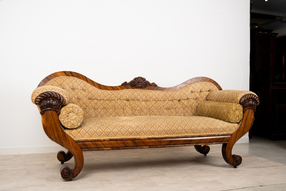 A Victorian rosewood settee featuring carved scroll ends, a central carved cresting, and patterned mustard yellow upholstery with bolster cushions. View III