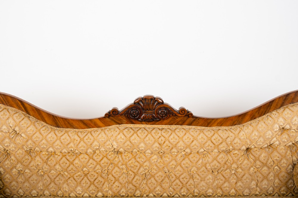 A Victorian rosewood settee featuring carved scroll ends, a central carved cresting, and patterned mustard yellow upholstery with bolster cushions. View VI