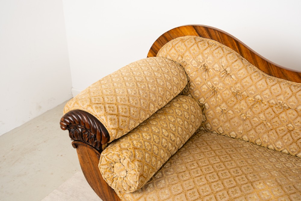 A Victorian rosewood settee featuring carved scroll ends, a central carved cresting, and patterned mustard yellow upholstery with bolster cushions. View VII