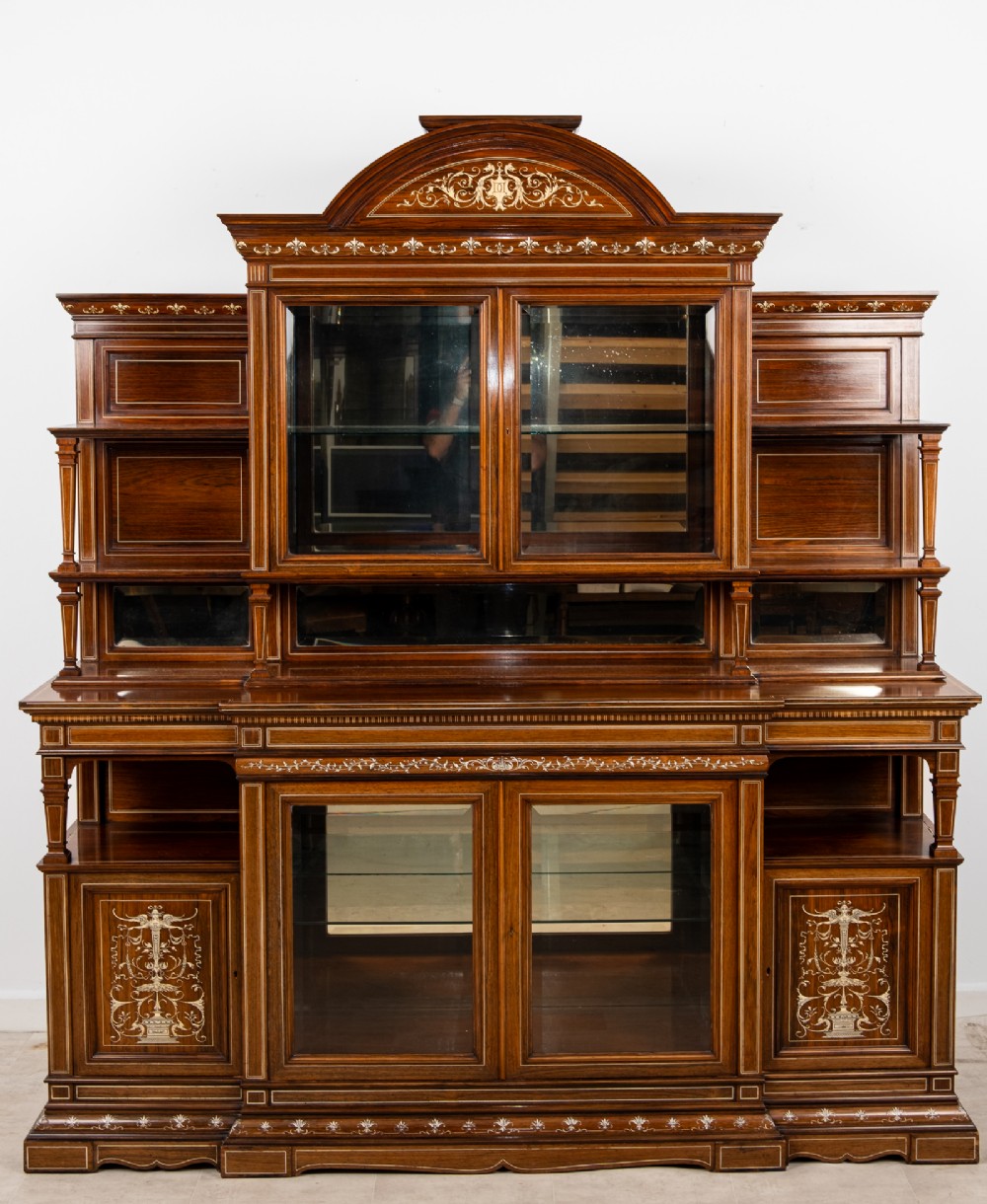 A monumental Victorian rosewood display cabinet featuring marquetry inlay, glazed doors, mirrored panels, and multi-tiered shelving. View V