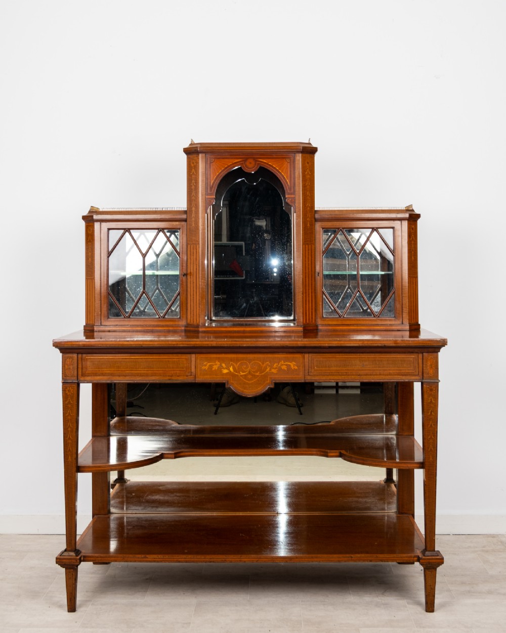 An Edwardian mahogany bonheur du jour writing desk featuring floral marquetry inlay, central mirrored recess, glazed side cabinets, and open lower shelves.