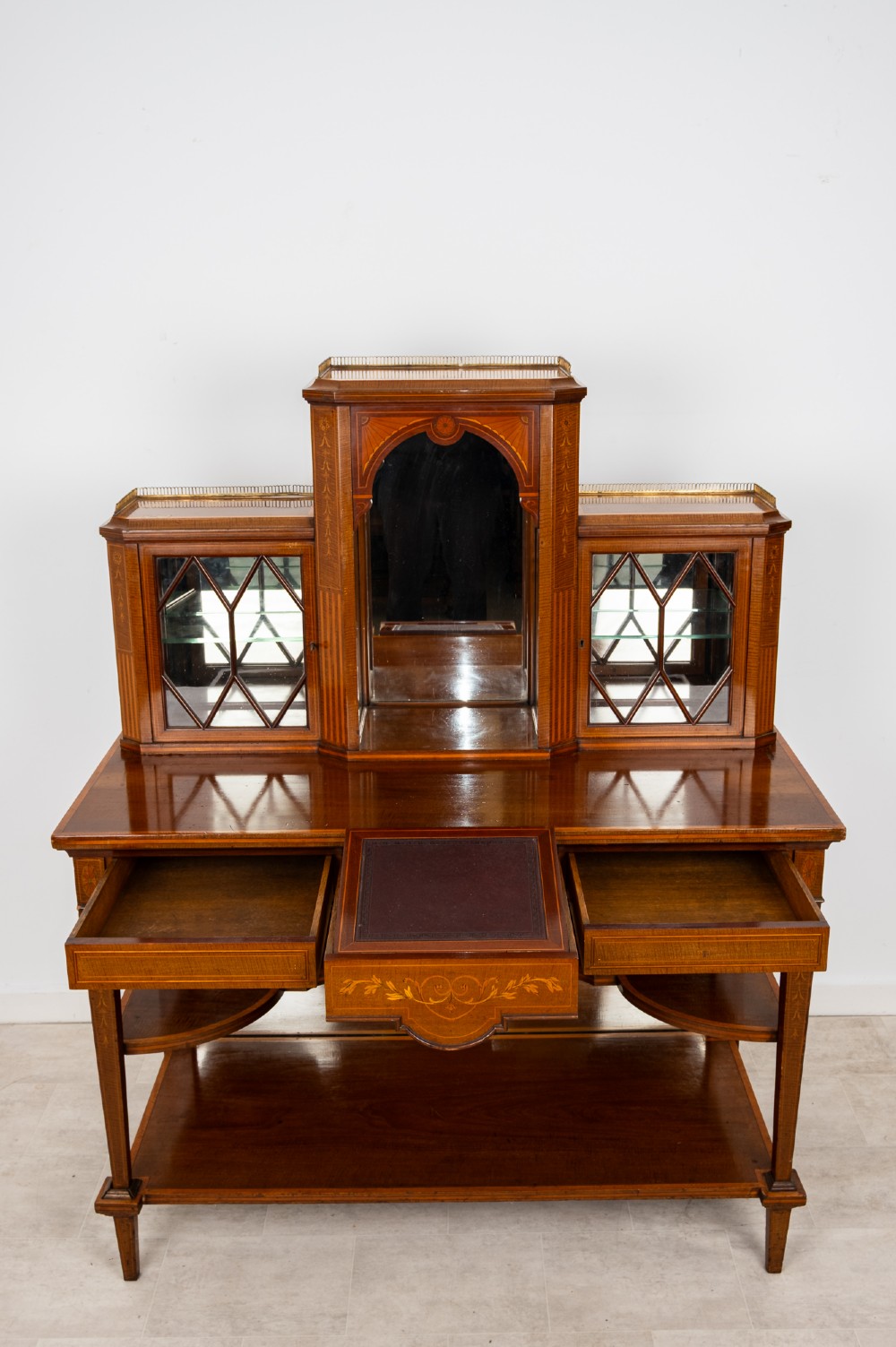 An Edwardian mahogany bonheur du jour writing desk featuring floral marquetry inlay, central mirrored recess, glazed side cabinets, and open lower shelves. View VI