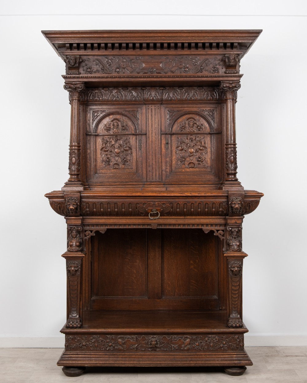 A 19th-century carved oak buffet cupboard featuring intricate relief panels, architectural columns, an upper cabinet, and an open lower tier.