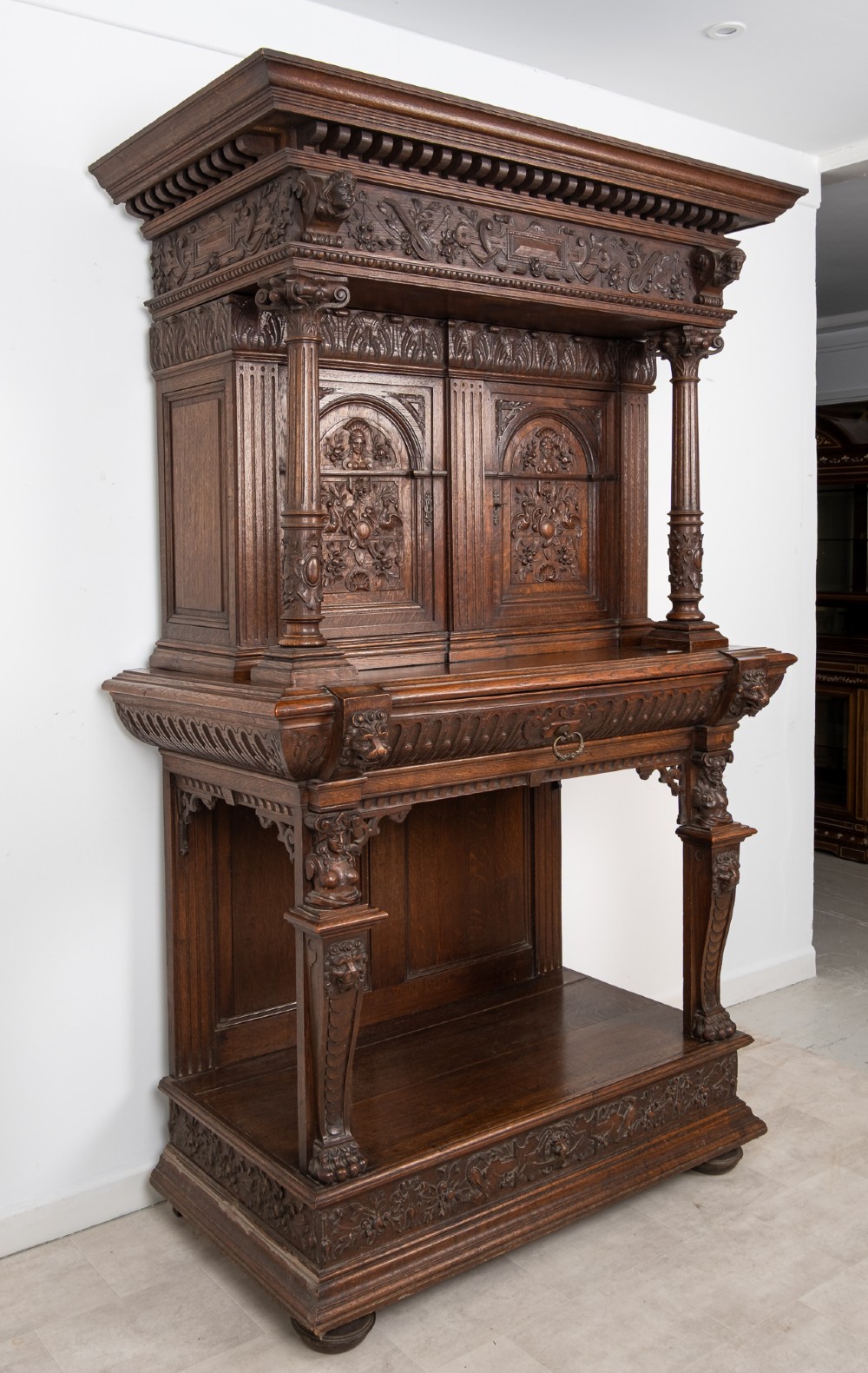 A 19th-century carved oak buffet cupboard featuring intricate relief panels, architectural columns, an upper cabinet, and an open lower tier. View XII