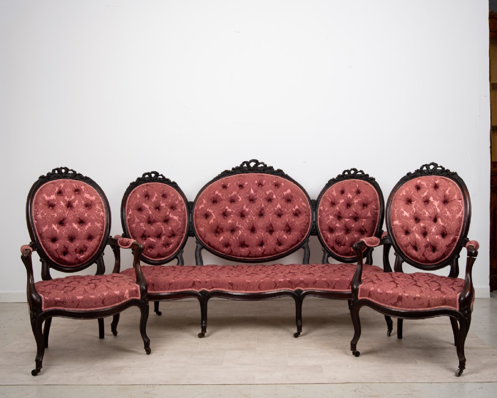 A three-piece Victorian mahogany salon suite featuring a three-back settee and two matching armchairs upholstered in rose-pink deep-buttoned fabric.