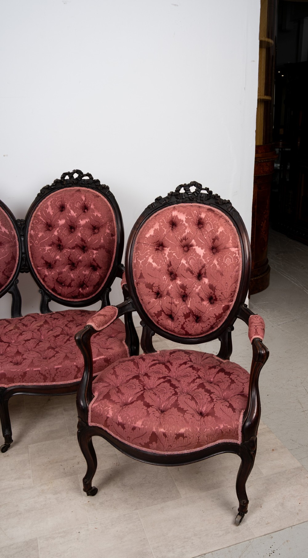 A three-piece Victorian mahogany salon suite featuring a three-back settee and two matching armchairs upholstered in rose-pink deep-buttoned fabric. View V