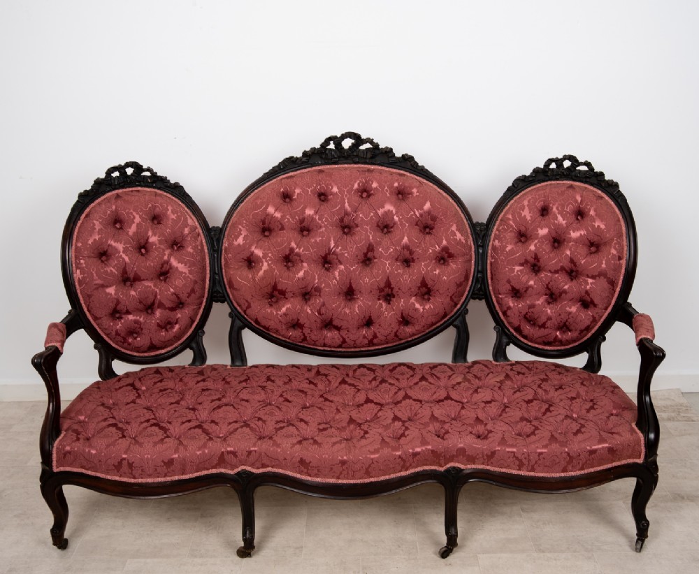 A three-piece Victorian mahogany salon suite featuring a three-back settee and two matching armchairs upholstered in rose-pink deep-buttoned fabric. View VII