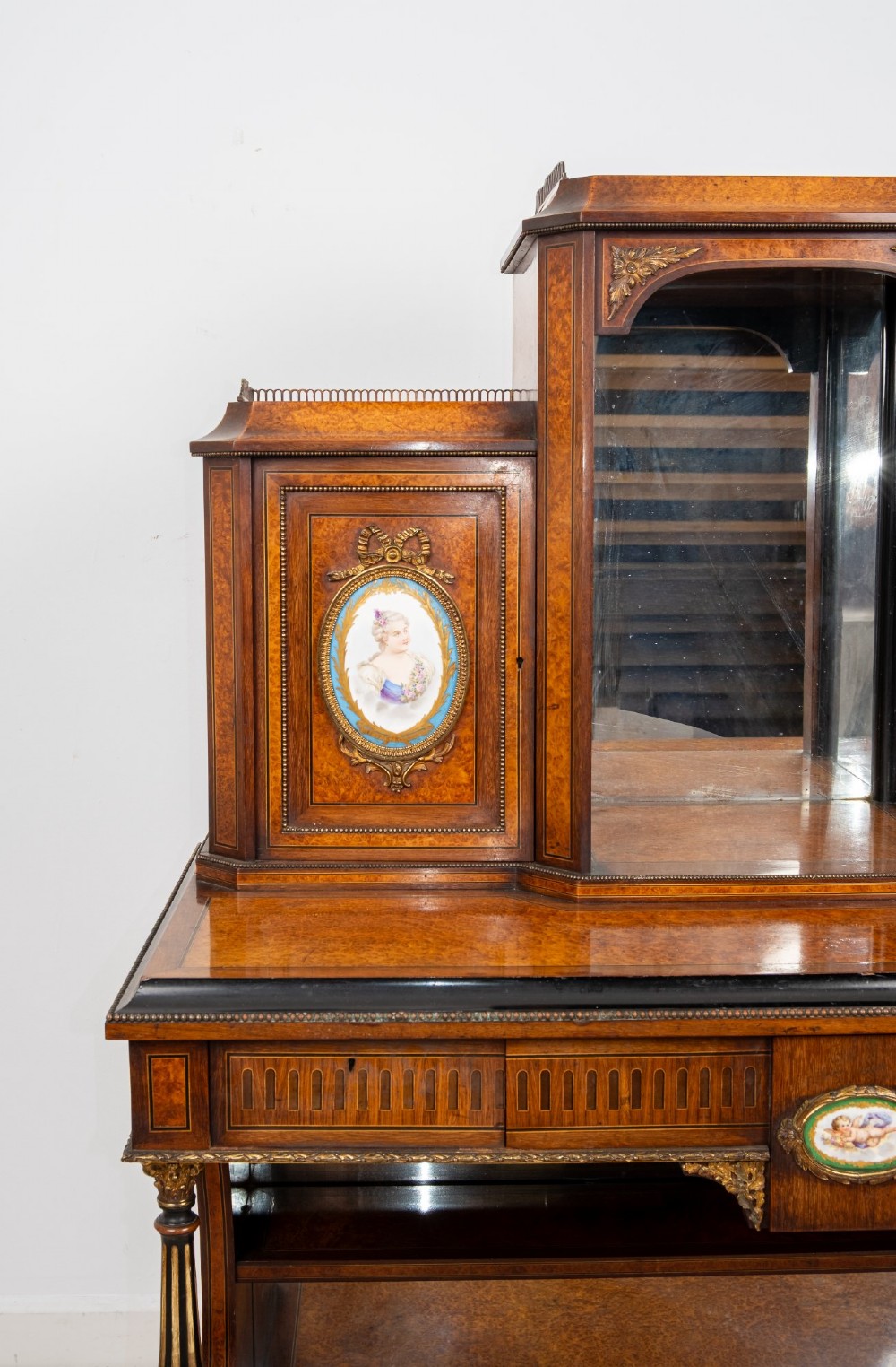 An antique French amboyna and ebonised bonheur du jour writing desk featuring inset porcelain plaques, gilt metal mounts, a central mirrored superstructure, and lower tier shelving. View V