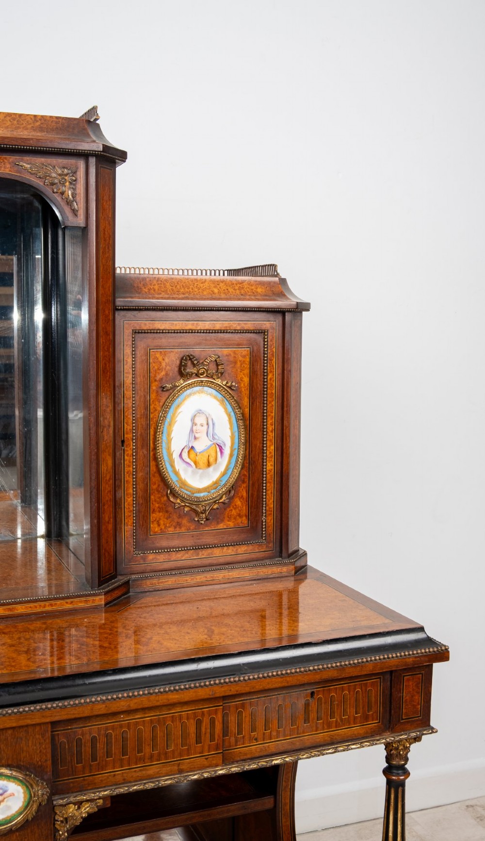 An antique French amboyna and ebonised bonheur du jour writing desk featuring inset porcelain plaques, gilt metal mounts, a central mirrored superstructure, and lower tier shelving. View VI