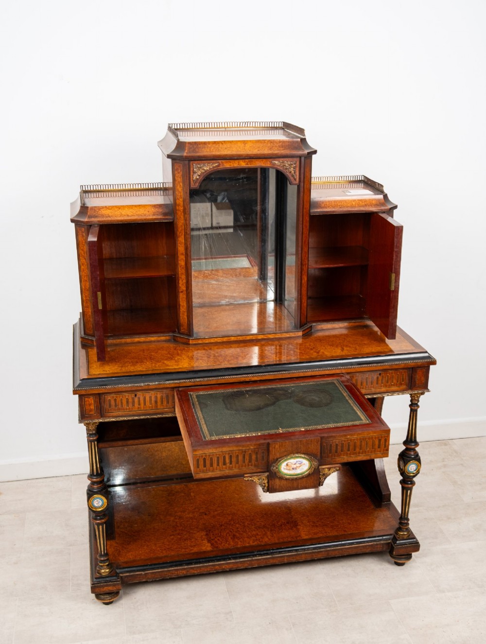 An antique French amboyna and ebonised bonheur du jour writing desk featuring inset porcelain plaques, gilt metal mounts, a central mirrored superstructure, and lower tier shelving. View VII