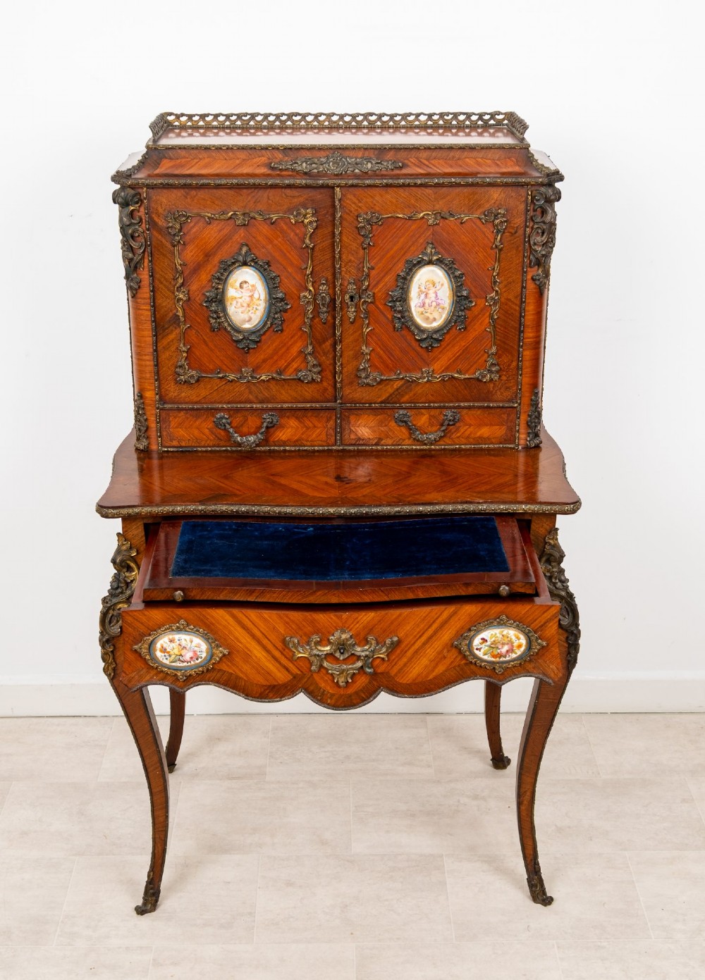 An antique French kingwood bonheur du jour writing desk featuring an upper cabinet with porcelain plaques, ornate ormolu mounts, and slender cabriole legs. View IX