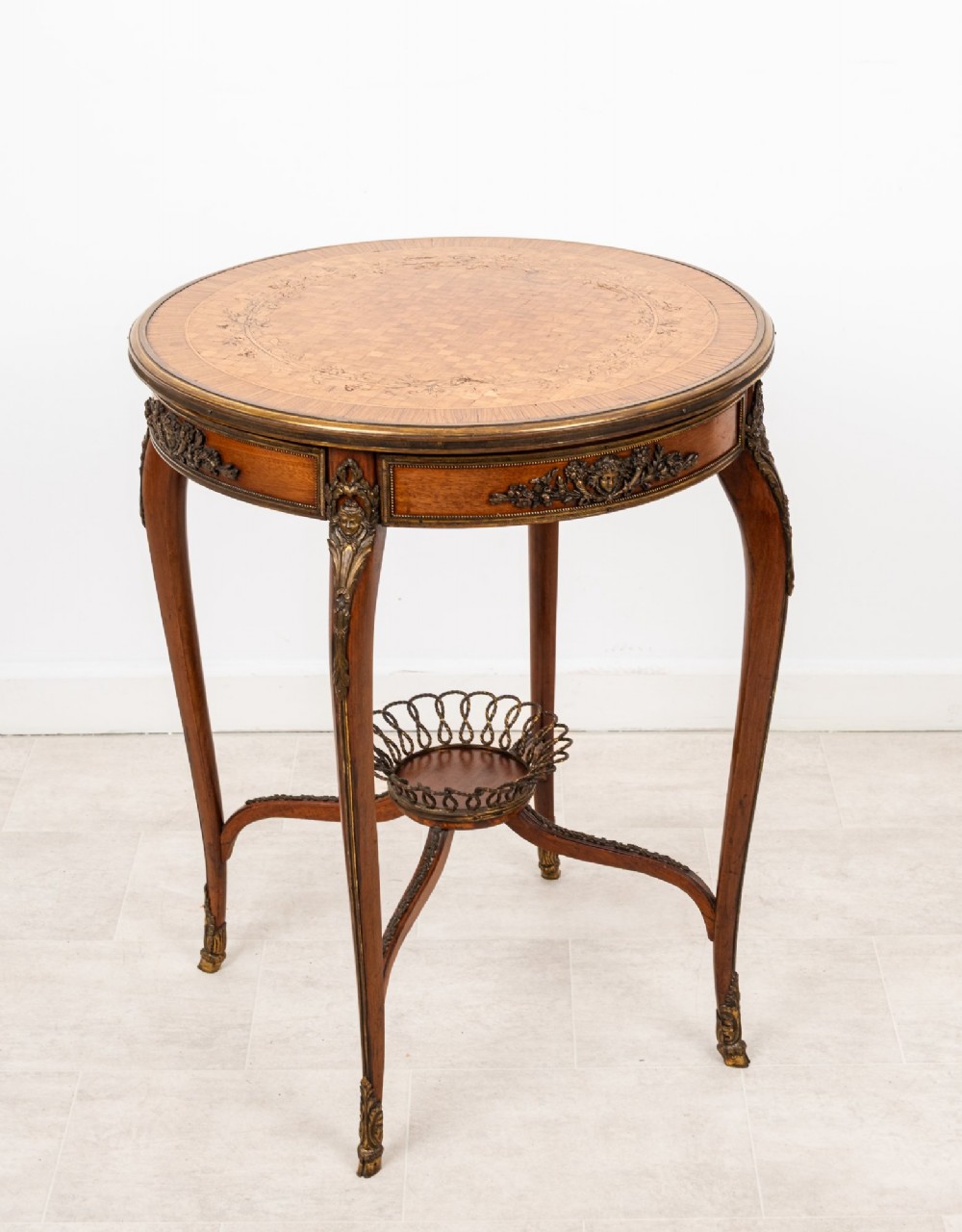 A circular French kingwood centre table featuring parquetry top inlay, gilt-bronze mounts, cabriole legs, and a central undertier basket.