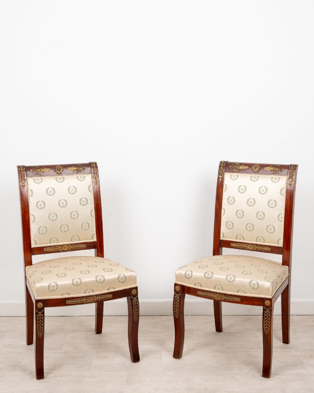 A pair of late 19th-century French Empire Revival mahogany side chairs featuring gilt-bronze ormolu mounts and cream upholstered seats and backrests.