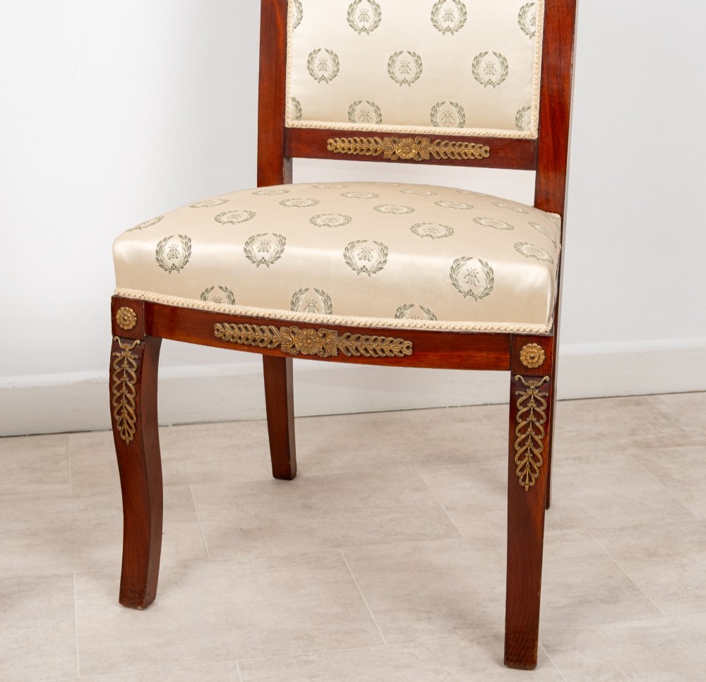 A pair of late 19th-century French Empire Revival mahogany side chairs featuring gilt-bronze ormolu mounts and cream upholstered seats and backrests. View V