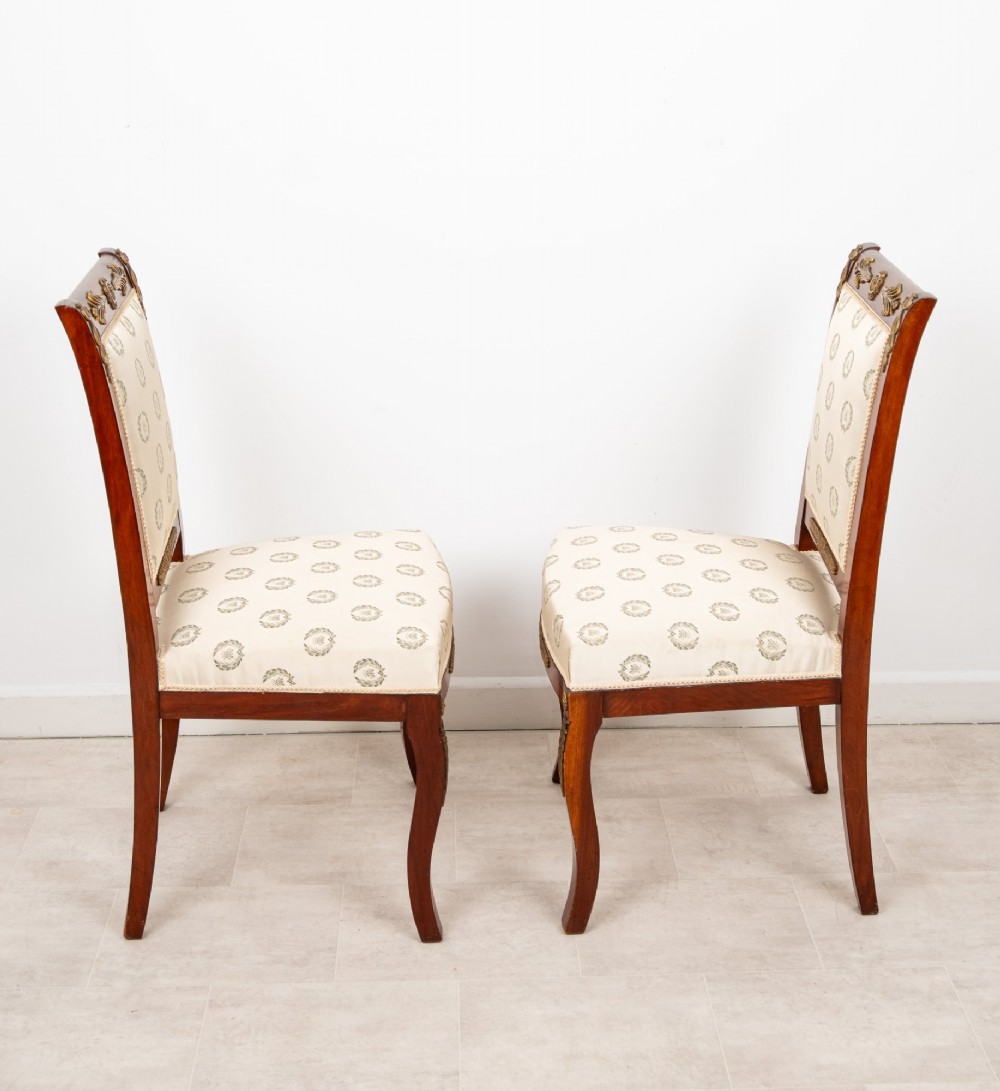 A pair of late 19th-century French Empire Revival mahogany side chairs featuring gilt-bronze ormolu mounts and cream upholstered seats and backrests. View VI