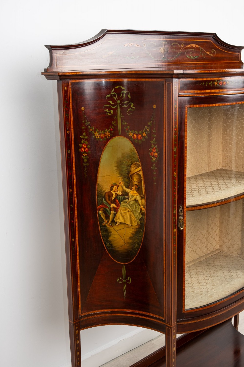 An Edwardian mahogany bow-front display cabinet featuring hand-painted classical scene panels, satinwood inlay, glass door, and tapered spade legs. View IV