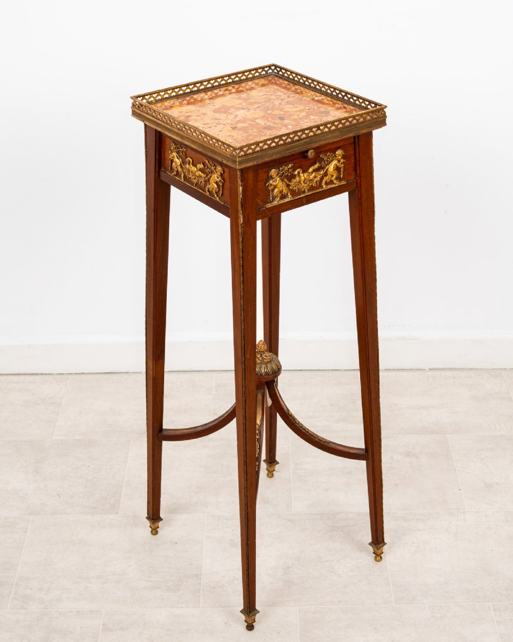 A tall French mahogany side table featuring a square rouge marble top with a pierced brass gallery, gilt-bronze frieze reliefs, and slender tapered legs connected by a curved stretcher.