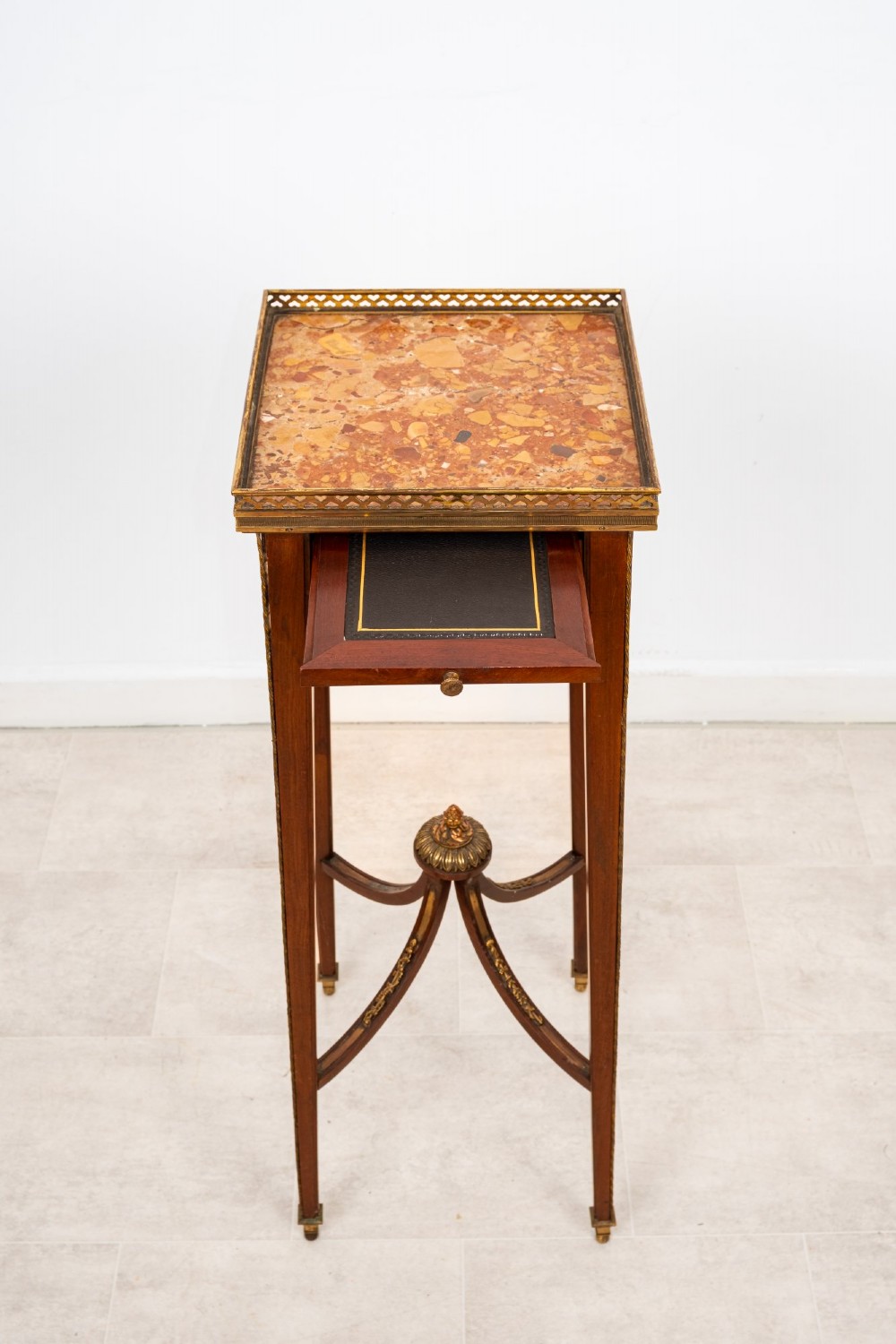 A tall French mahogany side table featuring a square rouge marble top with a pierced brass gallery, gilt-bronze frieze reliefs, and slender tapered legs connected by a curved stretcher. View VI