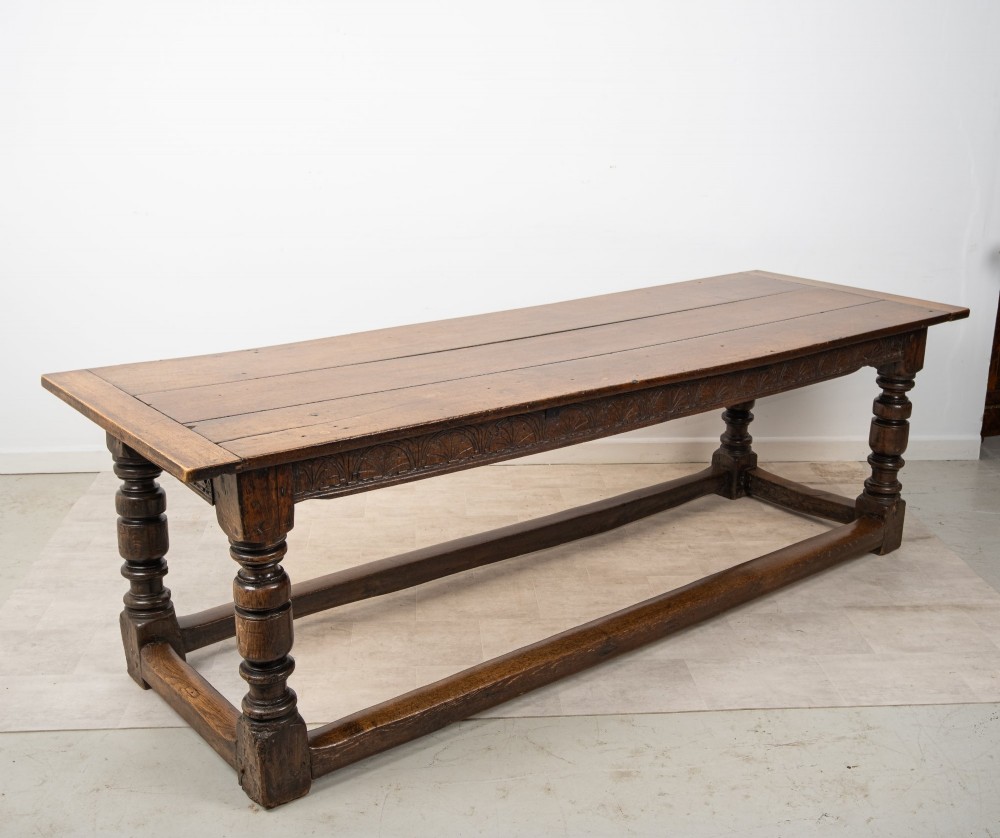 An 18th century carved oak refectory dining table featuring turned legs, a carved frieze apron, and low perimeter stretchers.