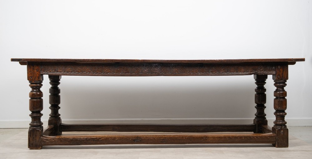 An 18th century carved oak refectory dining table featuring turned legs, a carved frieze apron, and low perimeter stretchers. View II