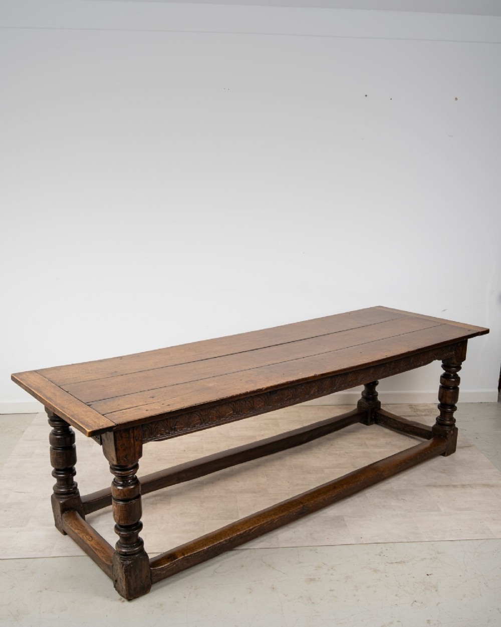 An 18th century carved oak refectory dining table featuring turned legs, a carved frieze apron, and low perimeter stretchers. View V
