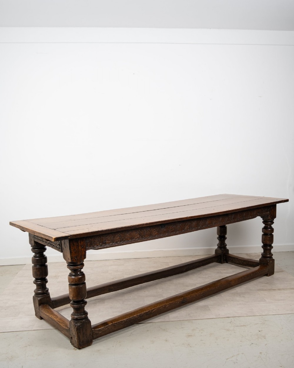 An 18th century carved oak refectory dining table featuring turned legs, a carved frieze apron, and low perimeter stretchers. View VI