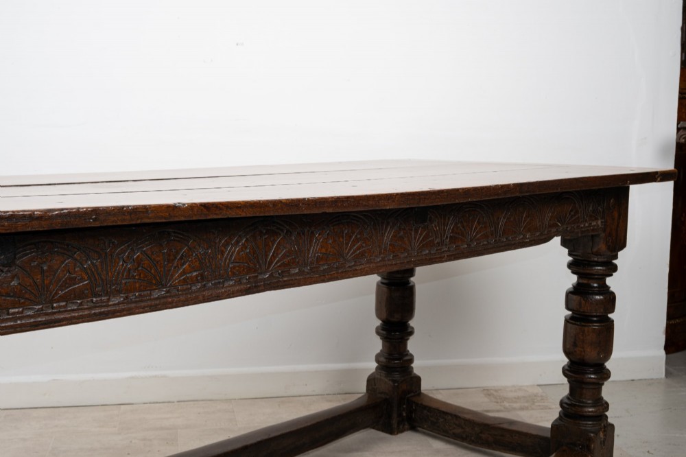An 18th century carved oak refectory dining table featuring turned legs, a carved frieze apron, and low perimeter stretchers. View VII