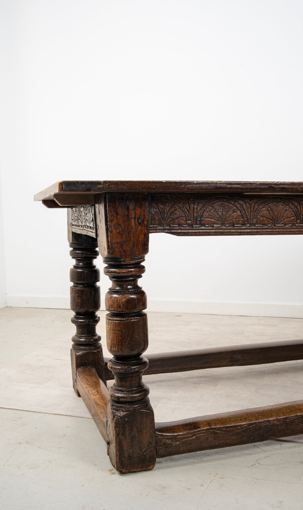 An 18th century carved oak refectory dining table featuring turned legs, a carved frieze apron, and low perimeter stretchers. View IX