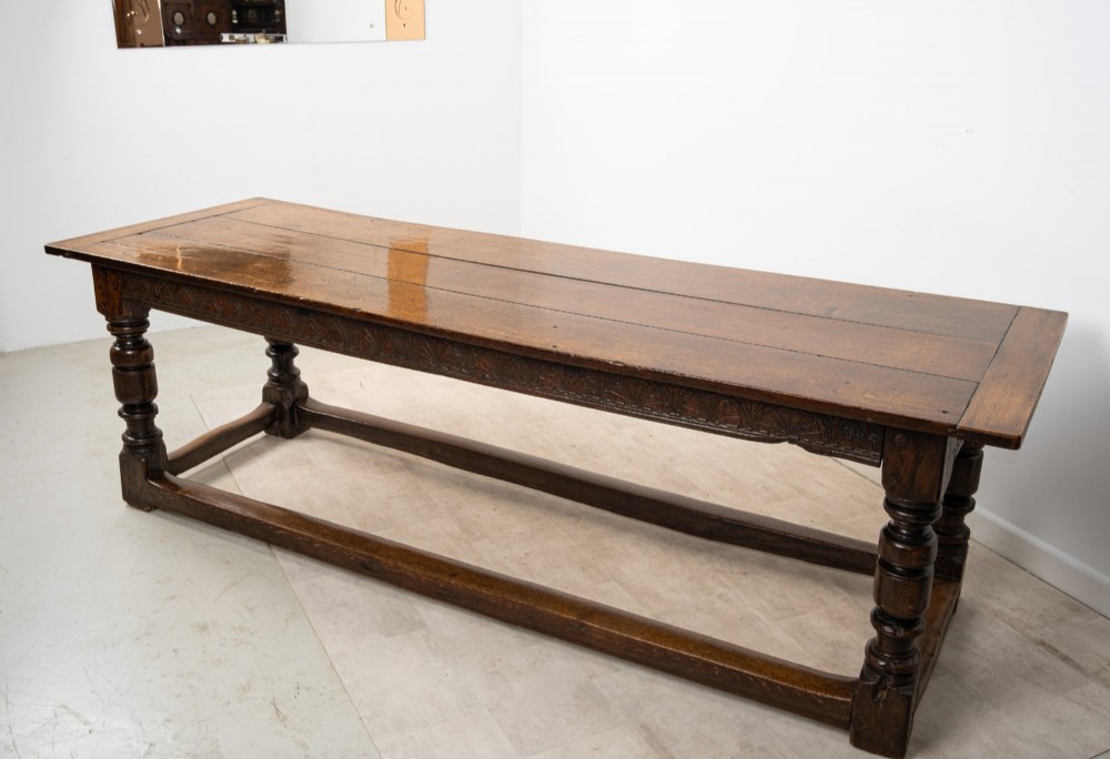 An 18th century carved oak refectory dining table featuring turned legs, a carved frieze apron, and low perimeter stretchers. View X
