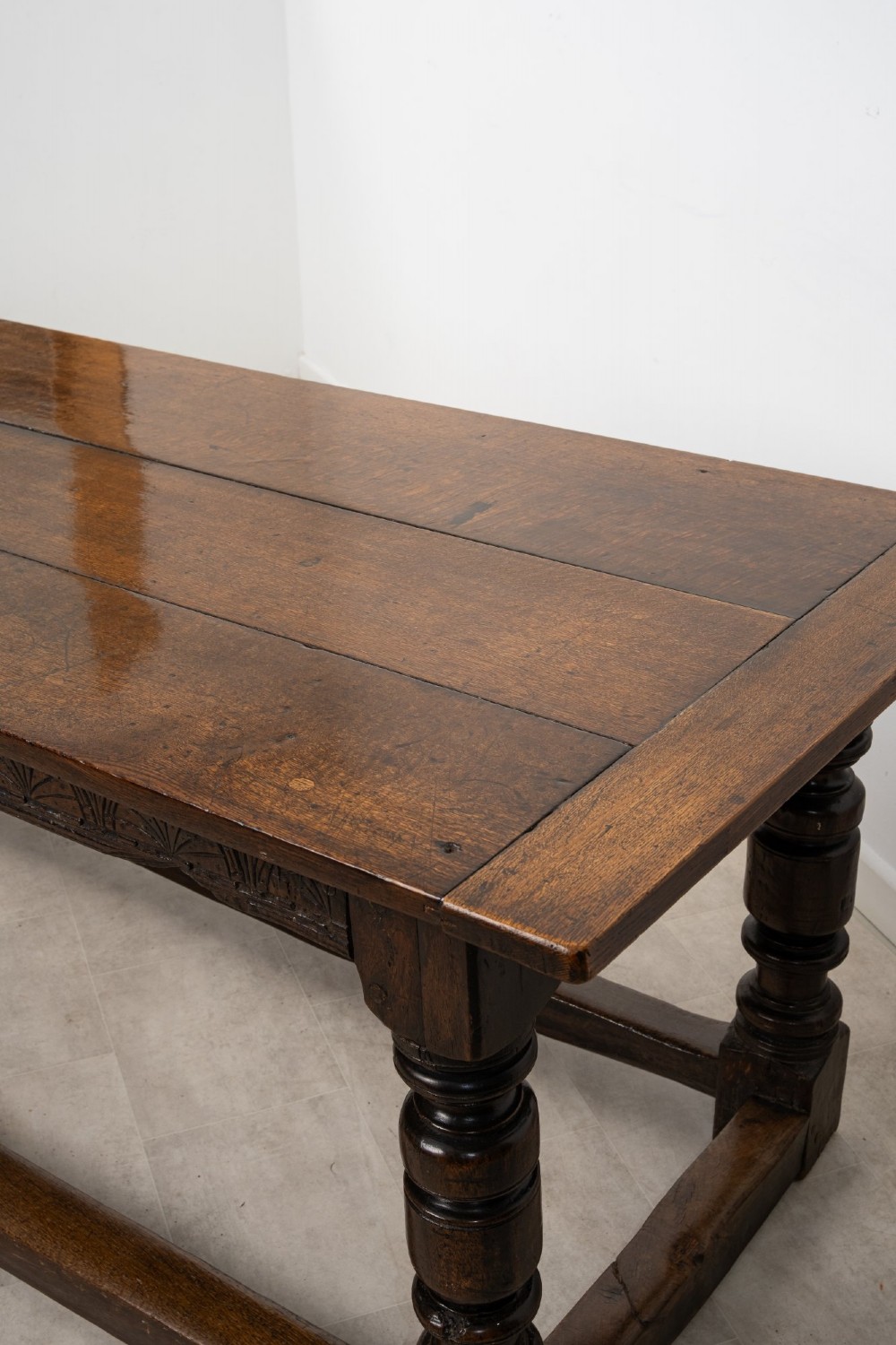 An 18th century carved oak refectory dining table featuring turned legs, a carved frieze apron, and low perimeter stretchers. View XII