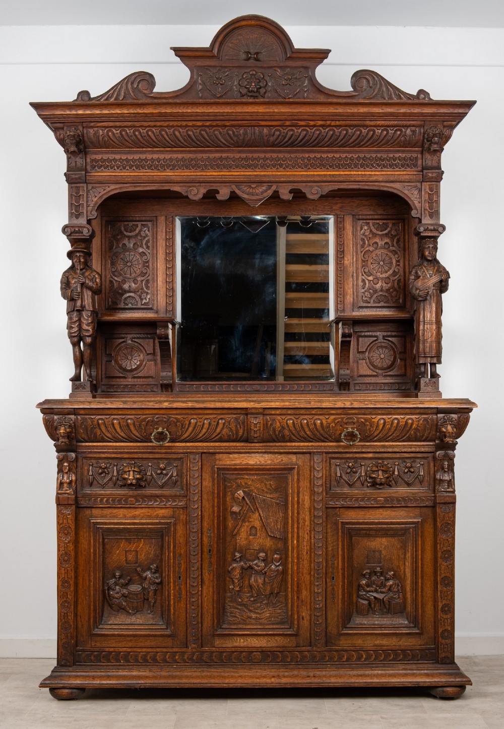 A late Victorian dark carved oak mirror-back sideboard featuring carved figural columns, relief panels, and a upper display shelf.
