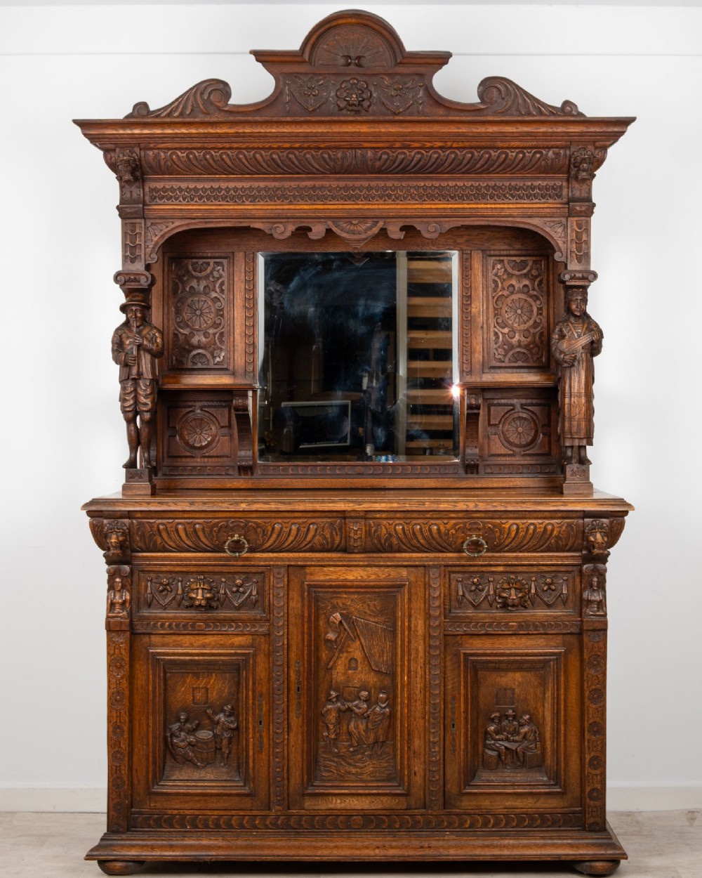 A late Victorian dark carved oak mirror-back sideboard featuring carved figural columns, relief panels, and a upper display shelf. View II