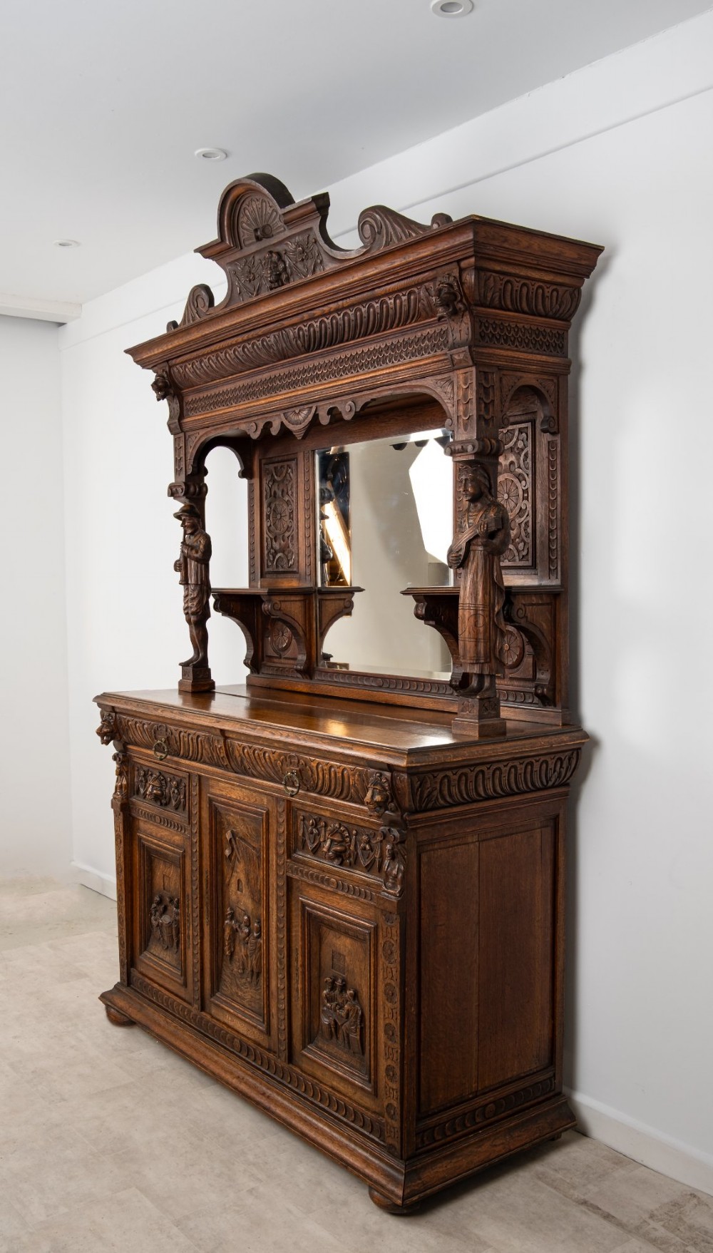 A late Victorian dark carved oak mirror-back sideboard featuring carved figural columns, relief panels, and a upper display shelf. View III