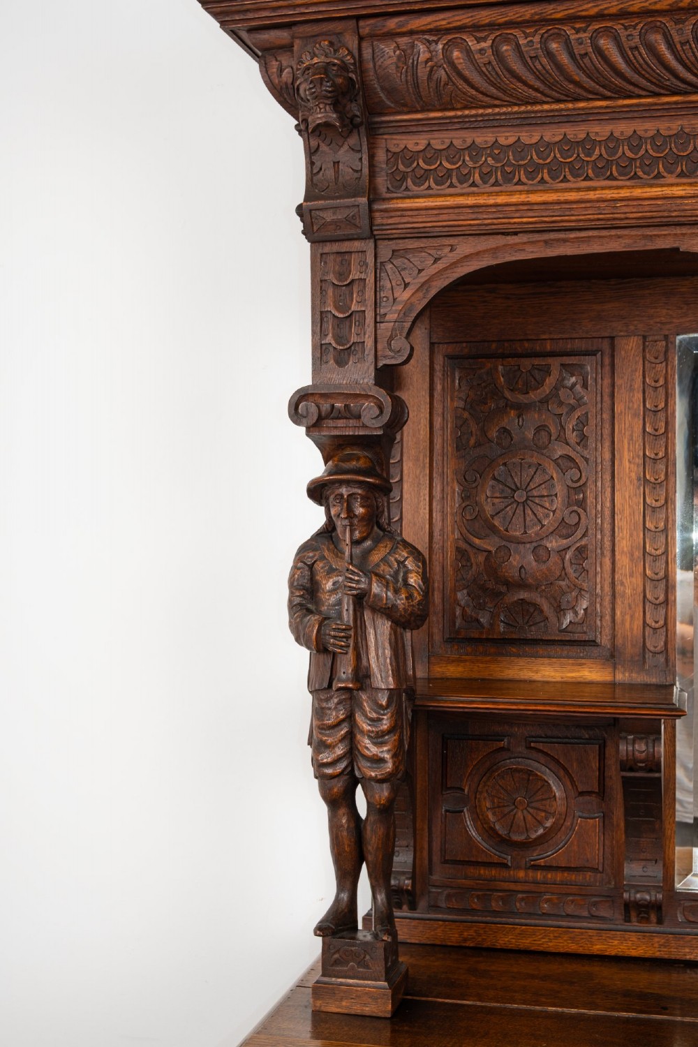 A late Victorian dark carved oak mirror-back sideboard featuring carved figural columns, relief panels, and a upper display shelf. View V