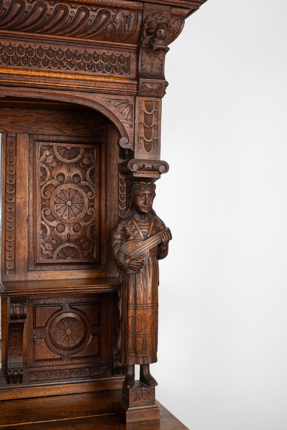 A late Victorian dark carved oak mirror-back sideboard featuring carved figural columns, relief panels, and a upper display shelf. View VI