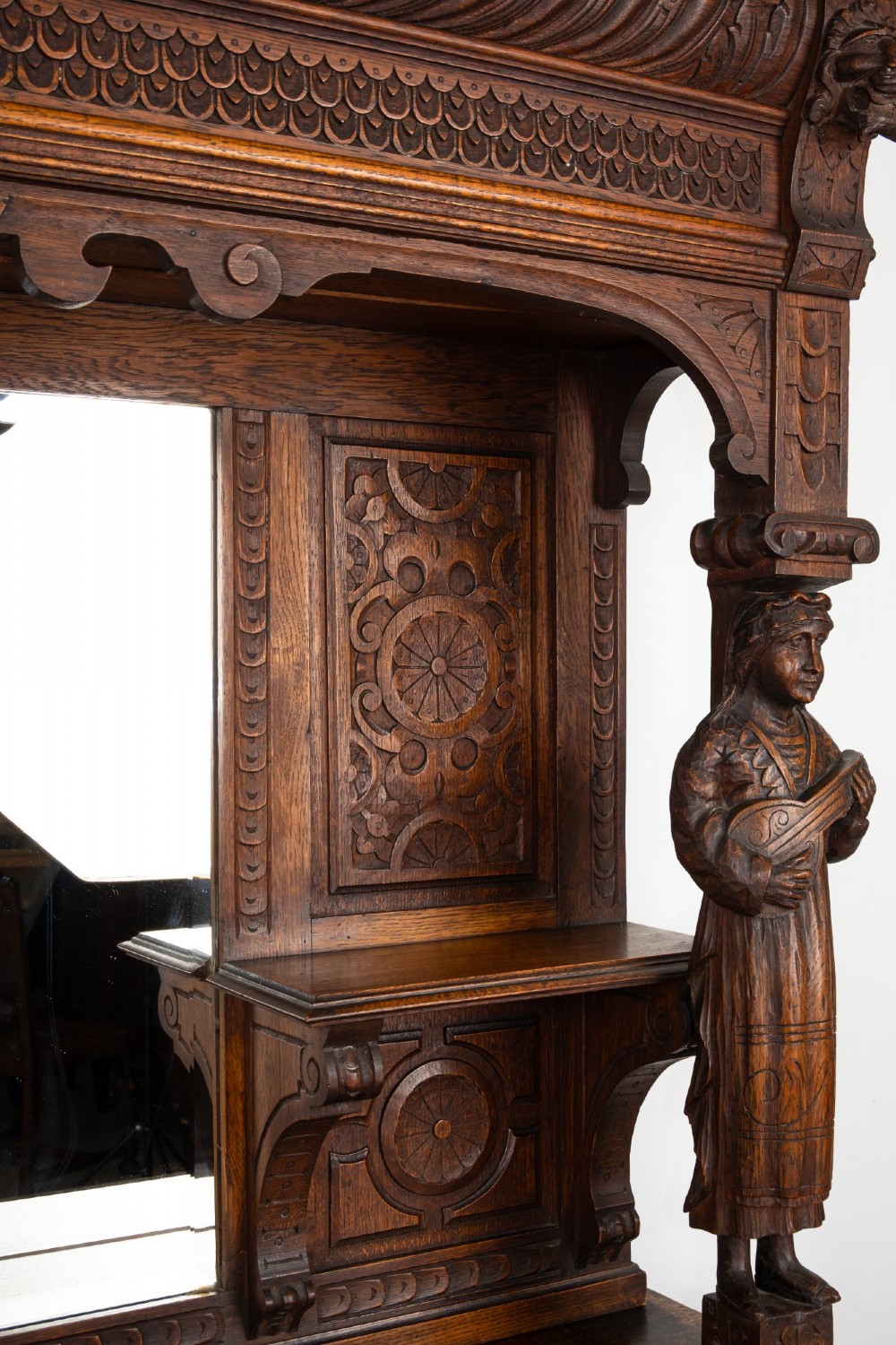 A late Victorian dark carved oak mirror-back sideboard featuring carved figural columns, relief panels, and a upper display shelf. View VIII