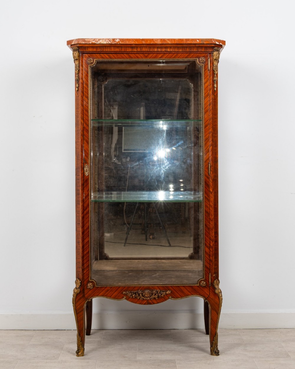 An antique French Louis XV style kingwood vitrine cabinet featuring a single glazed door, gilt-bronze mounts, a mirrored back interior, glass shelves, and a marble top.