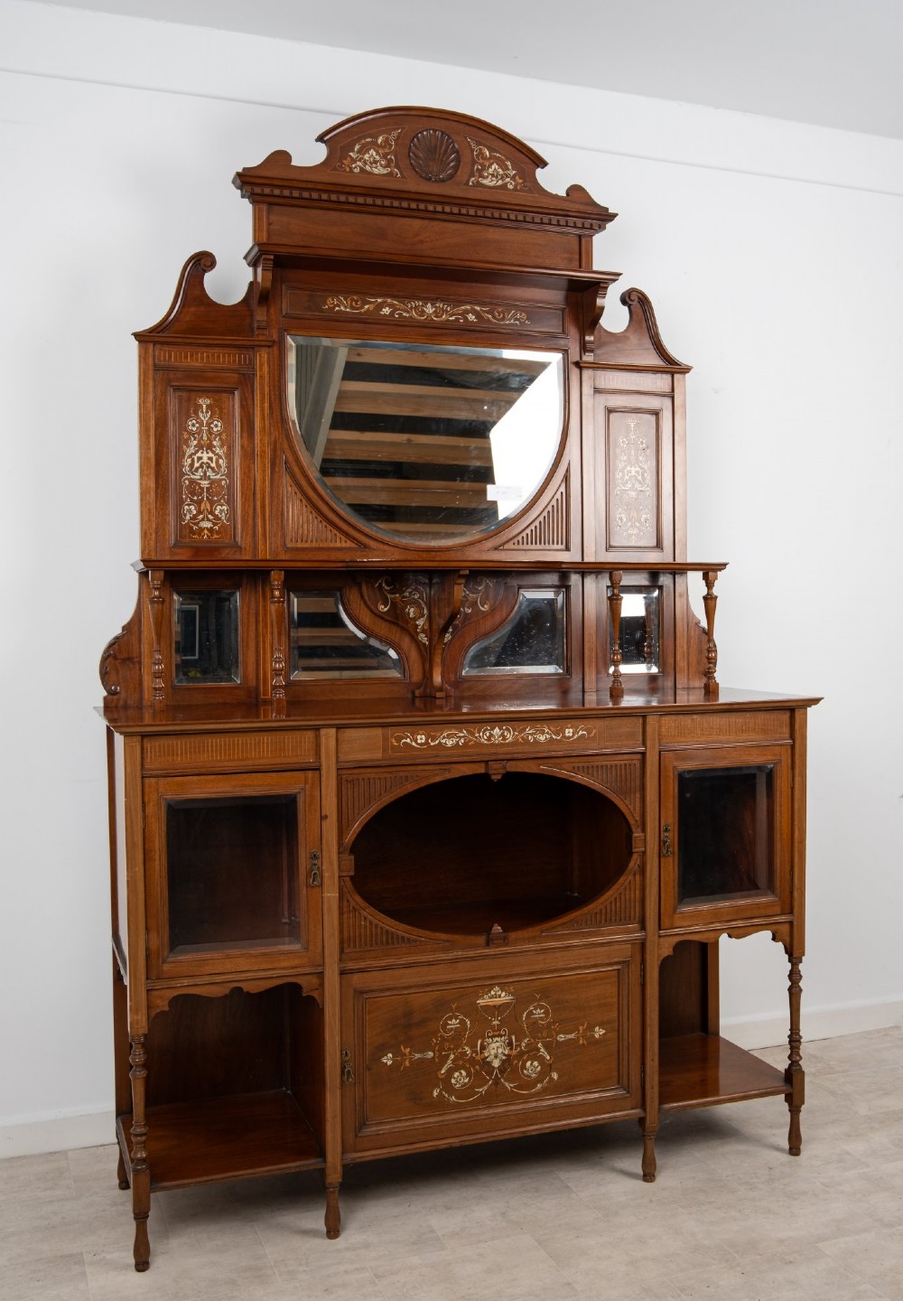 A late Victorian mahogany chiffonier cabinet featuring floral marquetry inlay, glass cupboard doors, open lower shelving, and an upper oval mirror back with a carved shell crest. View III