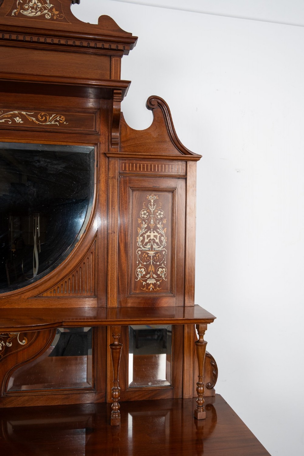 A late Victorian mahogany chiffonier cabinet featuring floral marquetry inlay, glass cupboard doors, open lower shelving, and an upper oval mirror back with a carved shell crest. View V