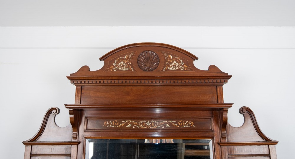 A late Victorian mahogany chiffonier cabinet featuring floral marquetry inlay, glass cupboard doors, open lower shelving, and an upper oval mirror back with a carved shell crest. View VI