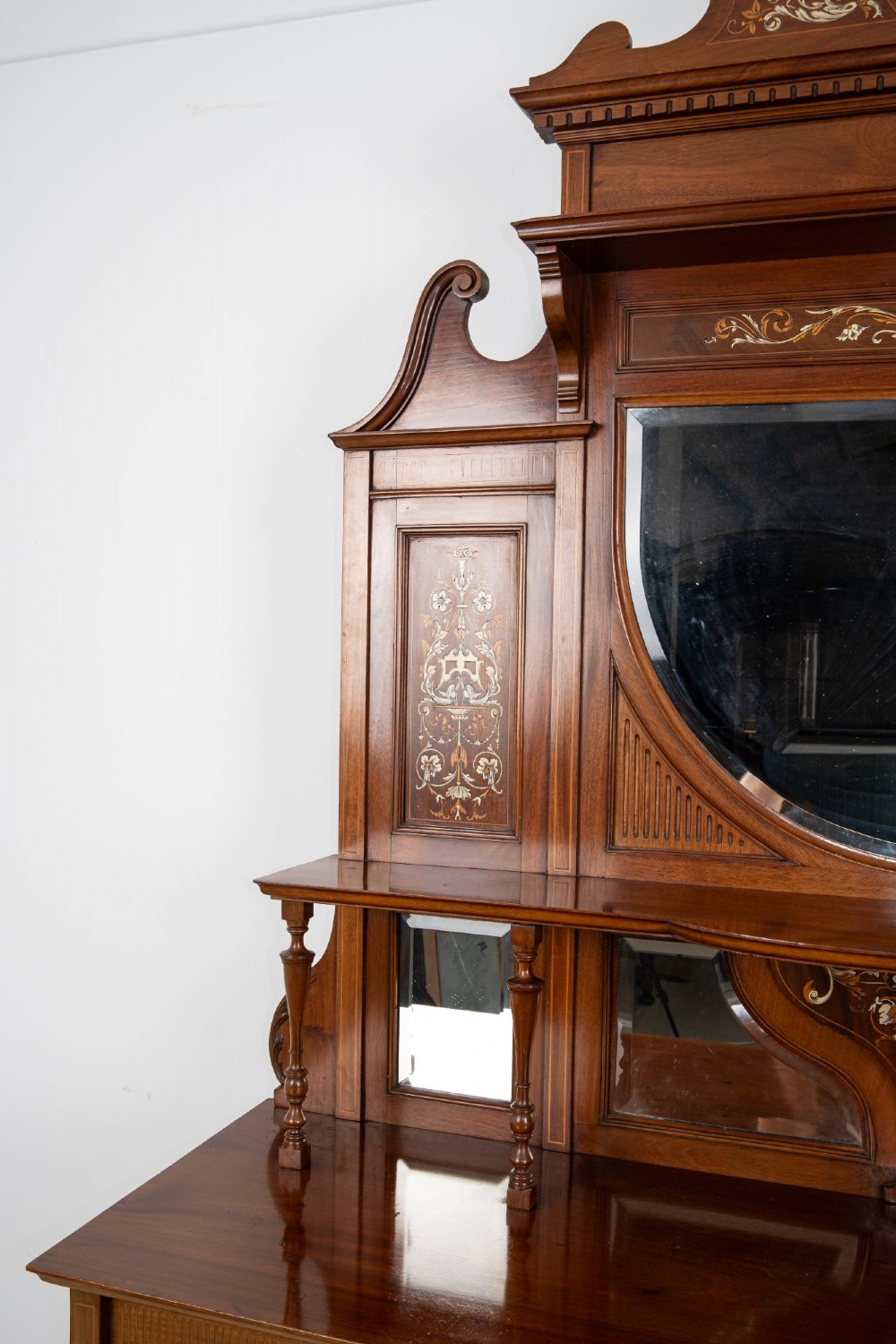 A late Victorian mahogany chiffonier cabinet featuring floral marquetry inlay, glass cupboard doors, open lower shelving, and an upper oval mirror back with a carved shell crest. View VII
