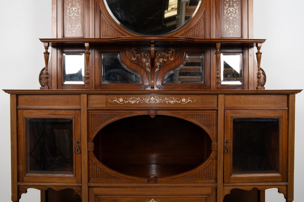 A late Victorian mahogany chiffonier cabinet featuring floral marquetry inlay, glass cupboard doors, open lower shelving, and an upper oval mirror back with a carved shell crest. View VIII