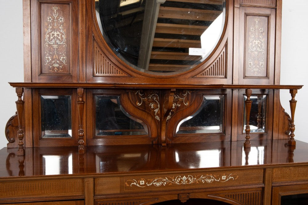 A late Victorian mahogany chiffonier cabinet featuring floral marquetry inlay, glass cupboard doors, open lower shelving, and an upper oval mirror back with a carved shell crest. View IX