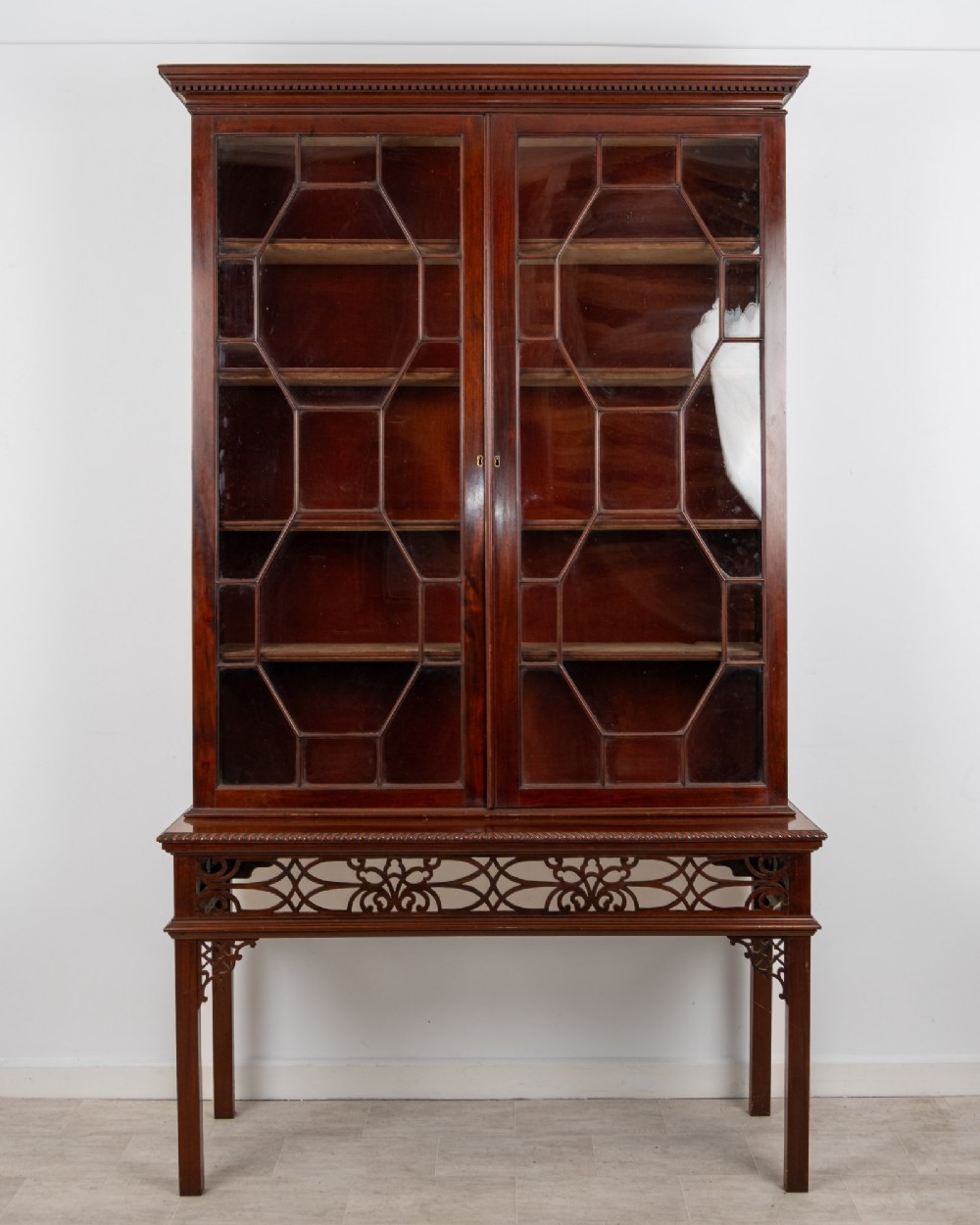 An antique mahogany astragal glazed bookcase resting on a carved matching stand with fretwork detailing.