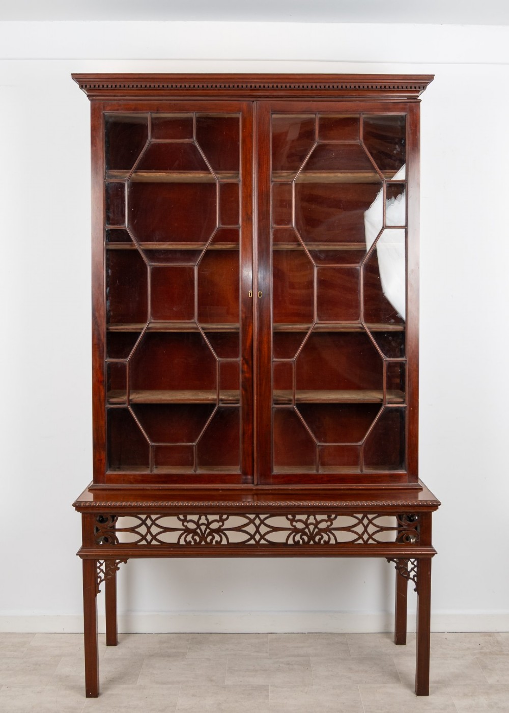 An antique mahogany astragal glazed bookcase resting on a carved matching stand with fretwork detailing. View II