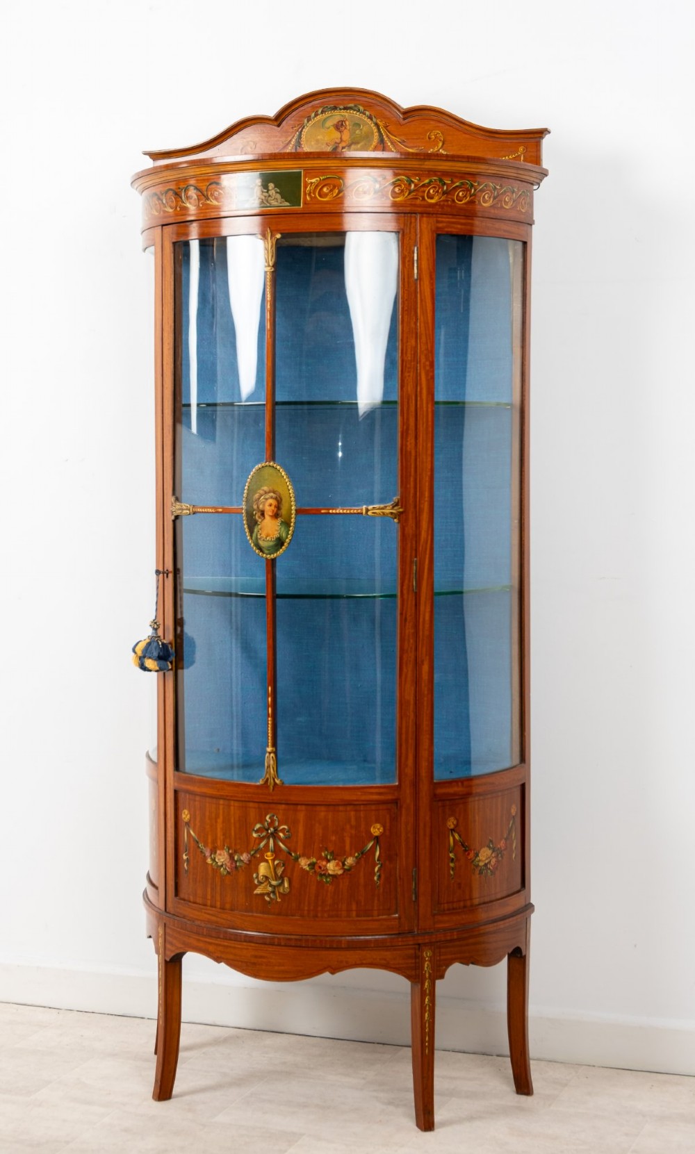 An Edwardian satinwood bow-front vitrine display cabinet featuring hand-painted floral swags, a central painted portrait medallion, curved glass panels, and a blue fabric-lined interior. View III