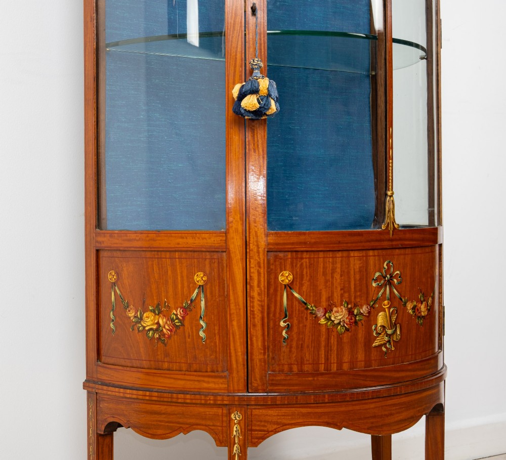 An Edwardian satinwood bow-front vitrine display cabinet featuring hand-painted floral swags, a central painted portrait medallion, curved glass panels, and a blue fabric-lined interior. View VII