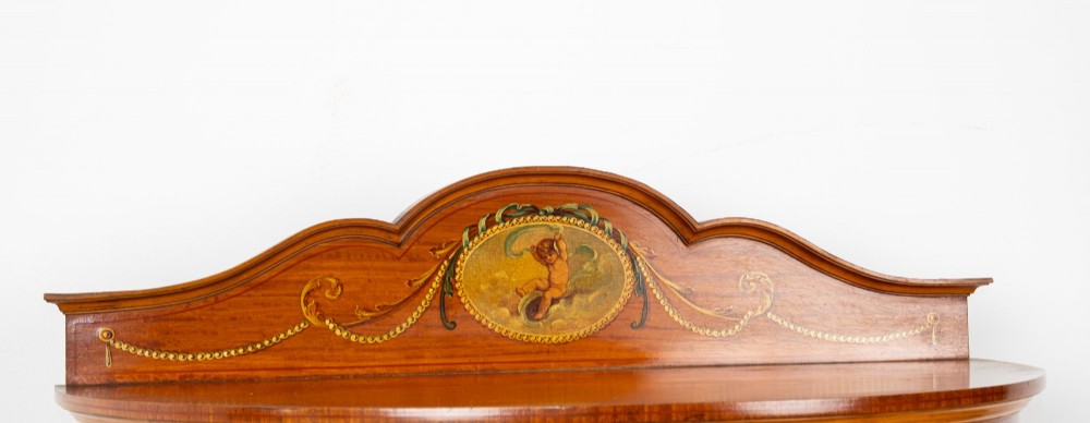 An Edwardian satinwood bow-front vitrine display cabinet featuring hand-painted floral swags, a central painted portrait medallion, curved glass panels, and a blue fabric-lined interior. View VIII