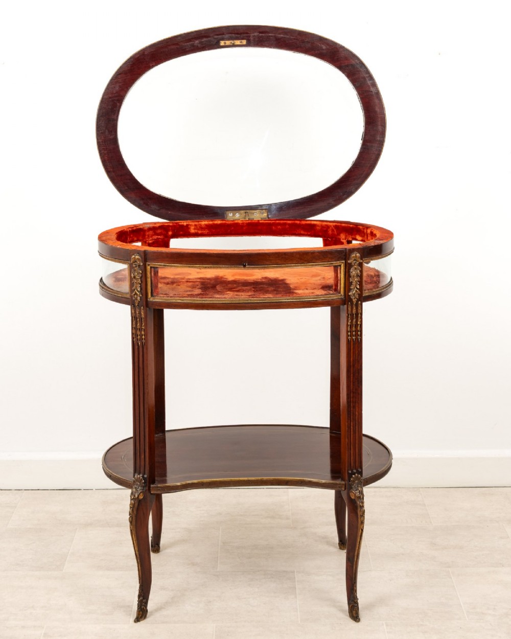 An antique oval mahogany bijouterie table featuring curved glass sides, an undertier shelf, and ornate gilt-bronze mounts. View III