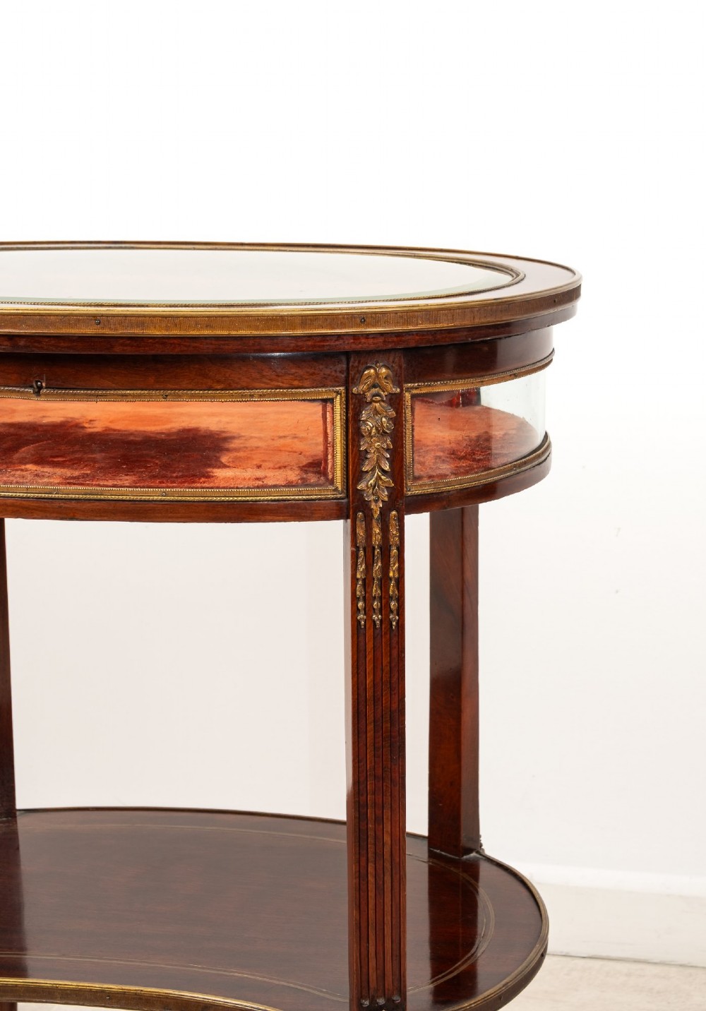 An antique oval mahogany bijouterie table featuring curved glass sides, an undertier shelf, and ornate gilt-bronze mounts. View IV